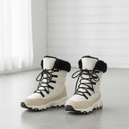 A pair of women's mid-calf lace-up winter boots in off-white and beige, featuring black faux-fur trim at the collar, black laces, and black outsole detailing, photographed on a light gray floor in a bright indoor setting.