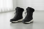 A pair of black winter lace-up boots with plush faux-fur trim at the collar, shown on a light gray floor against a white paneled wall.