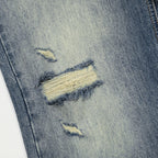Close-up of a distressed denim fabric with tears and frayed edges.