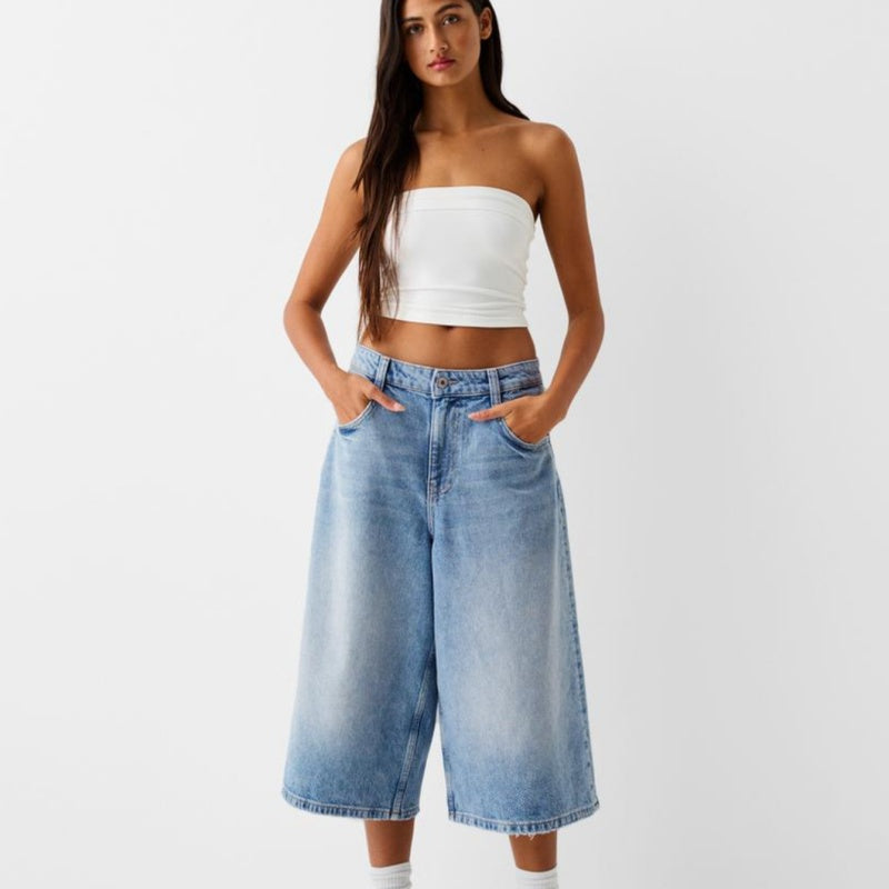 Woman wearing a white strapless top and blue denim wide-leg pants on a plain background