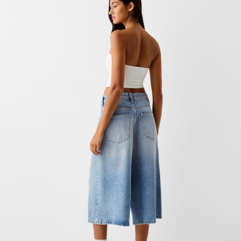 Woman wearing a white top and blue denim skirt on a light gray background