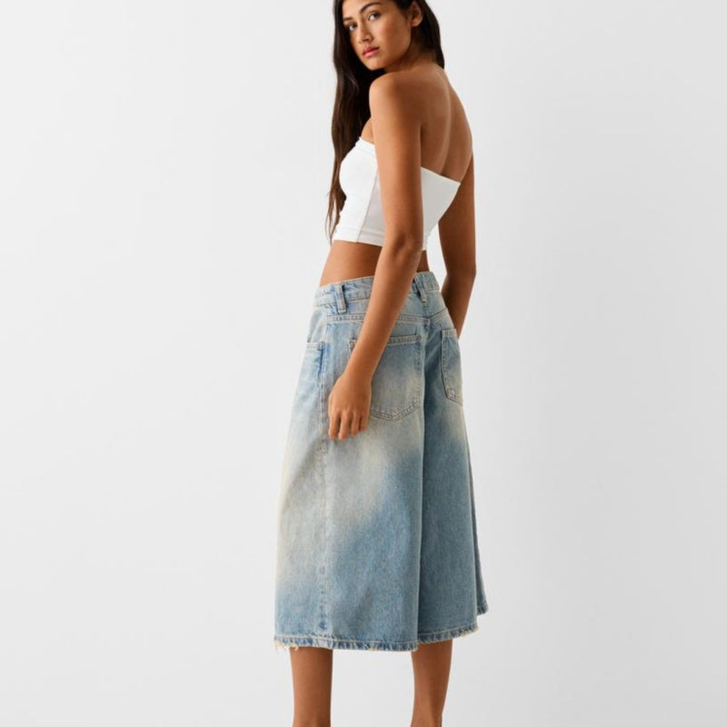 Woman wearing a white crop top and denim skirt on a plain background